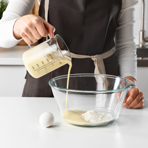 A person pours liquid from a measuring jug into a bowl, demonstrating its function for precise measurement in baking.