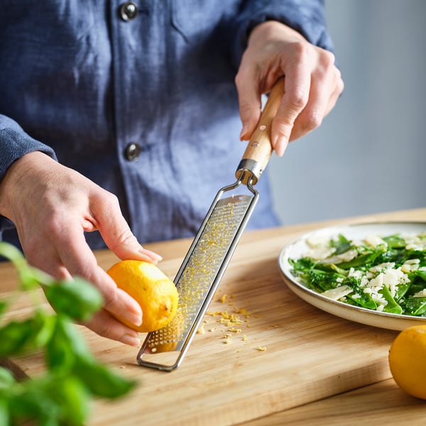 Person zests lemon on wooden cutting board beside salad bowl. VARDAGEN citrus zester used.