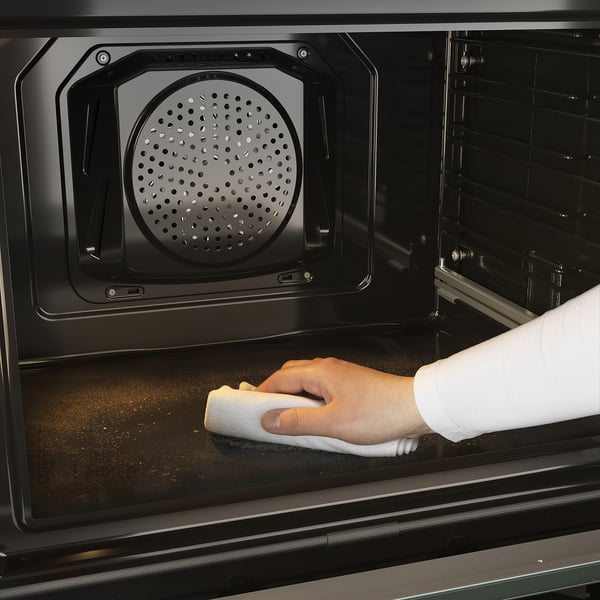 Person cleans oven with cloth. Modern self-cleaning oven sleek design and easy-to-use touch controls.