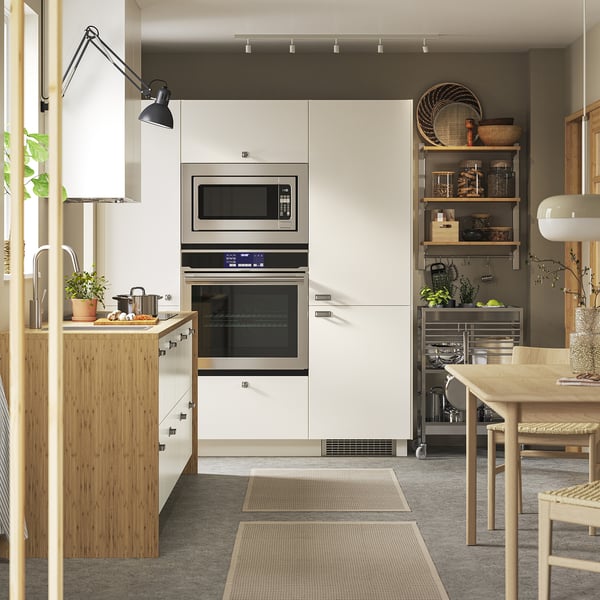 Modern kitchen with VEDDINGE white cabinets, wooden accents, stainless steel appliances, plants, and wooden dining table.
