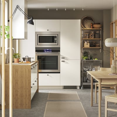 Modern kitchen with VEDDINGE white cabinets, wooden accents, stainless steel appliances, plants, and wooden dining table.