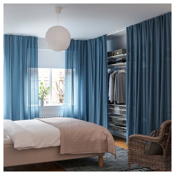 Blue curtains with white hooks hang near a bed. A pendant lamp dangles above, and a basket sits beside the bed.
