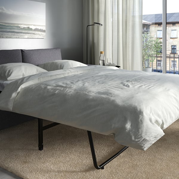 Modern bedroom with twin beds and a large window. Beds have stylish, grey headrests and white linens.