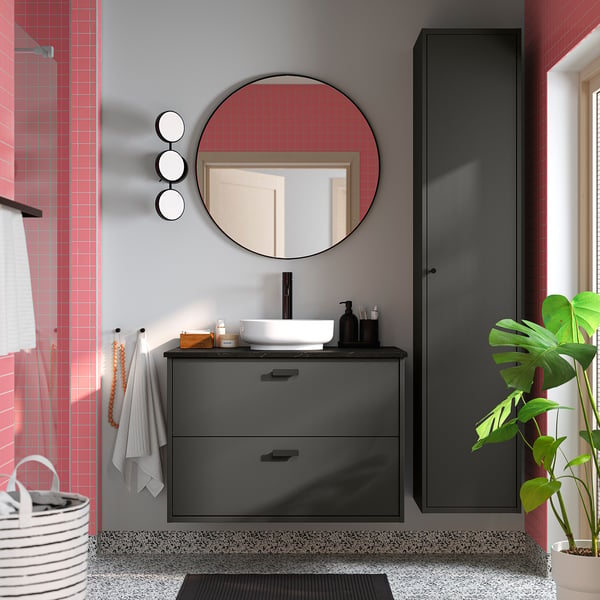 Modern bathroom with grey VINDELÄLVEN countertop sink, round mirror, black accents, red tiled wall, and green plant.