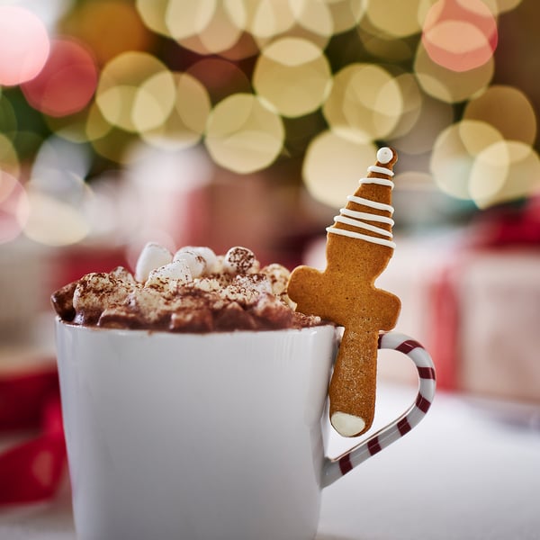 A festive mug filled with hot cocoa, topped with marshmallows and a gingerbread elf decoration.