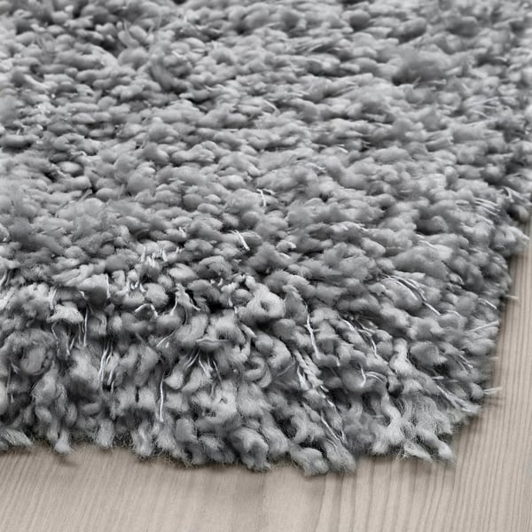 Close-up a shaggy, textured rug. Thick, soft pile with varied yarn thickness, lying on wooden floor.