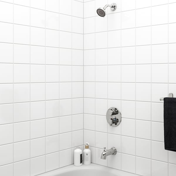Minimalist bathroom with chrome shower, white tiles, two bottles, black towel.