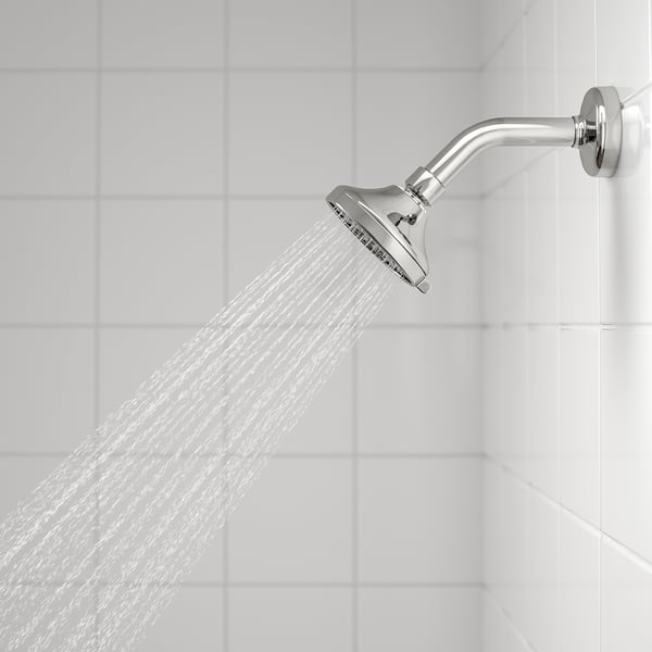 Showerhead in action, water flowing, chrome finish. Wide spray pattern on tiled bathroom wall.
