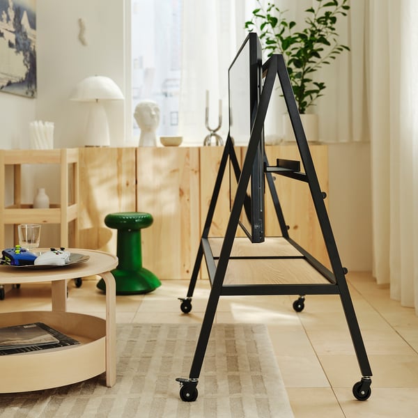 Black metal tv stand with wheels, holding a tv, positioned in a modern room. A wooden coffee table and decorative items are nearby.