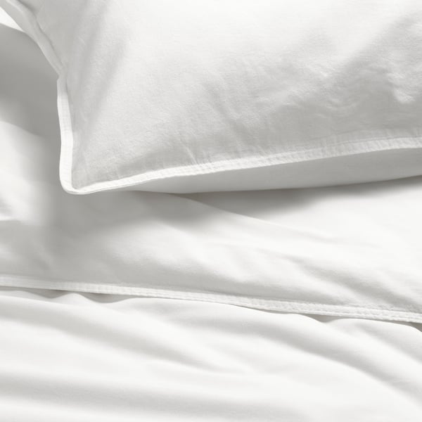 A cosy bed with a white, soft, high-quality, smooth cotton duvet and sheets. Sunlight casts gentle shadows on the bedding, highlighting its texture.