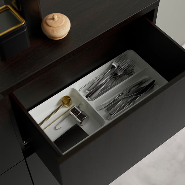 Open drawer with silverware compartments and small tools in a dark wooden cabinet.