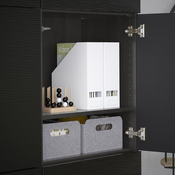 Black BESTÅ cabinet with adjustable shelves, holding white boxes and grey bins for organised storage. Doors feature soft-closing hinges.