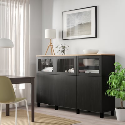 BESTÅ black glass storage unit between window & table, holding dishes, books, plant, & lamp. Picture above, lime cushion chair, bright room.
