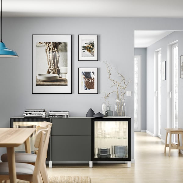 Modern living room with grey BESTÅ storage unit, wooden table, and chairs; glass doors, vases, and wall art.