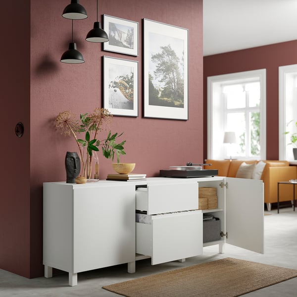 White BESTÅ storage unit with open doors, revealing adjustable shelves and drawers. Hanging artwork and flowers on top.