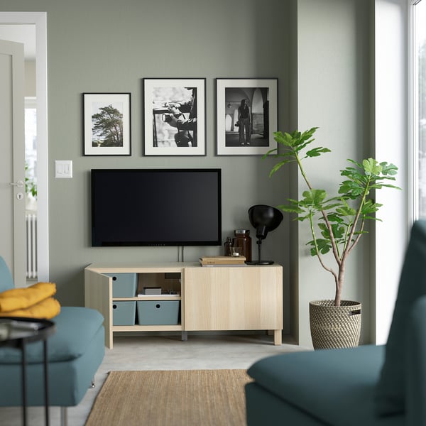 Modern living room with green walls and BESTÅ tv bench, adjustable shelves, three photos, tall plant in basket.