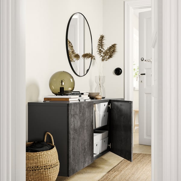 Modern hallway with black BESTÅ storage unit, white walls, round mirror, dried plants, lamp, and woven basket.