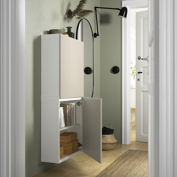 A tall white cabinet mounted on a green wall, with one door open exposing wicker baskets and folders, illustrating organised storage.