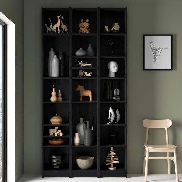 Large BILLY bookcase in dark wood with varied decor. Tall, filled with ornaments, vases, and figurines. Artwork and wooden chair nearby.
