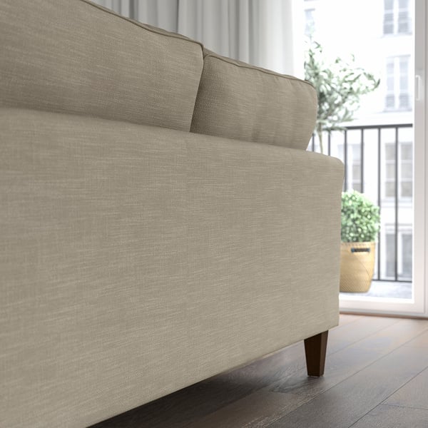 A beige EKHOLMA sofa with pocket springs for comfort, placed near a window. Its fitted cover is washable, ensuring easy maintenance.