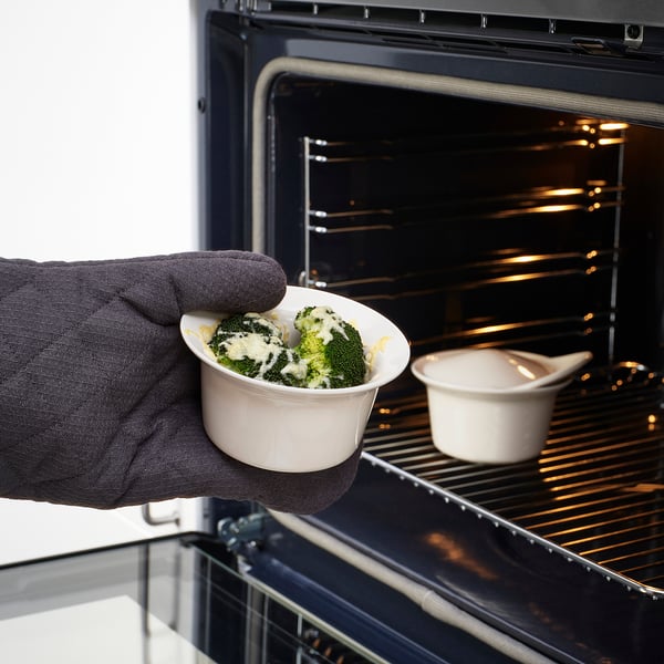 Hand holds dish with broccoli and cheese near oven, ready for baking.