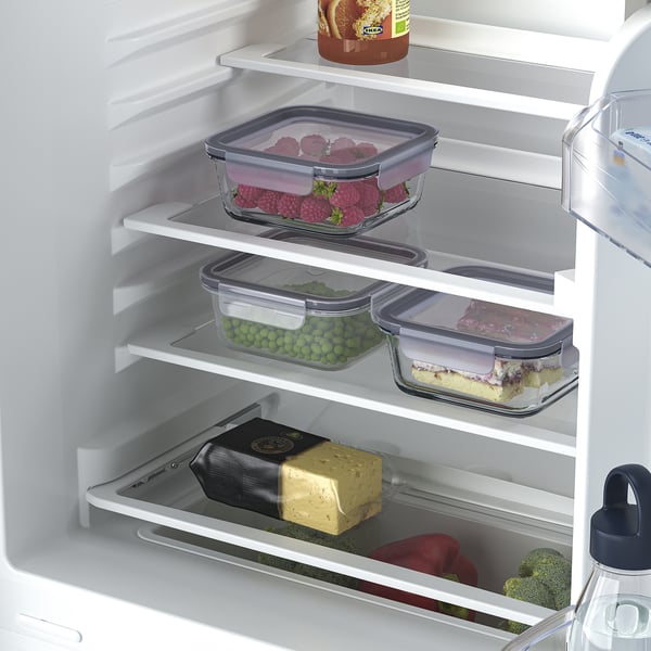 Fridge with adjustable glass shelves storing colourful fruits and vegetables, including raspberries and peas, along with butter and a cake.