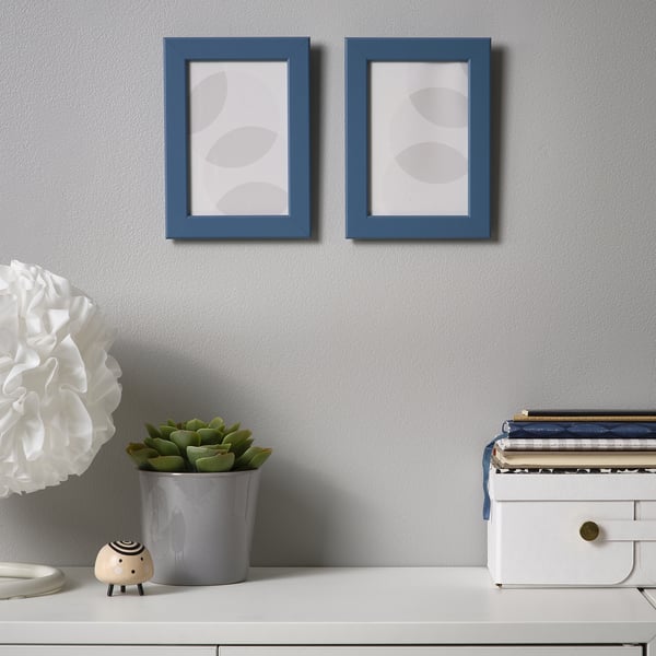 Blue frames on grey wall over desk with plant, elephant, lamp.