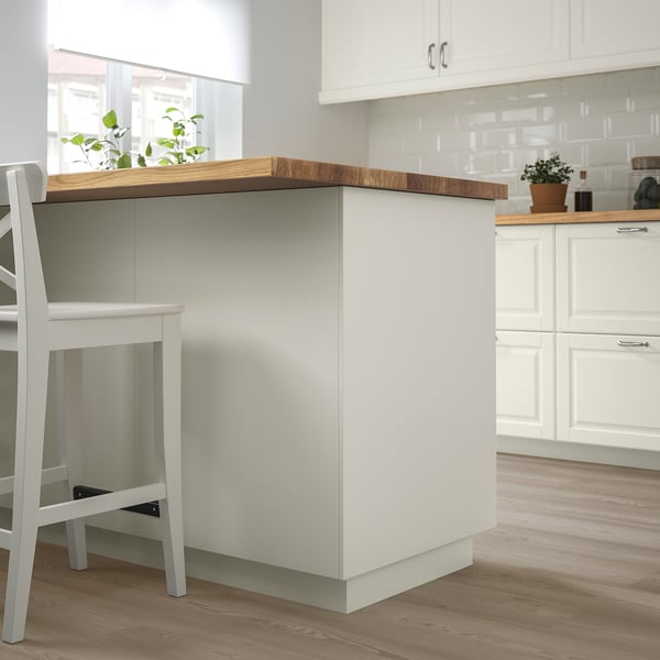 Modern kitchen with white FÖRBÄTTRA island, light wood tops, and sleek cabinets. Small plant accents add touch of green.