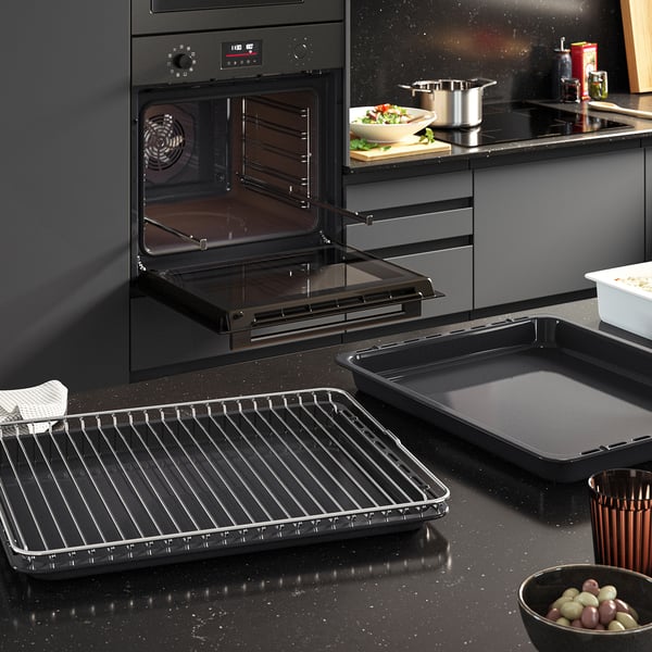 Modern black kitchen with open oven, racks, and grill pan, showcasing FRILLESBO ovens versatility for baking and grilling.