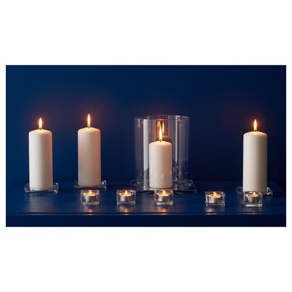 Four tall white candles in clear glass holders of different designs on a dark blue shelf.