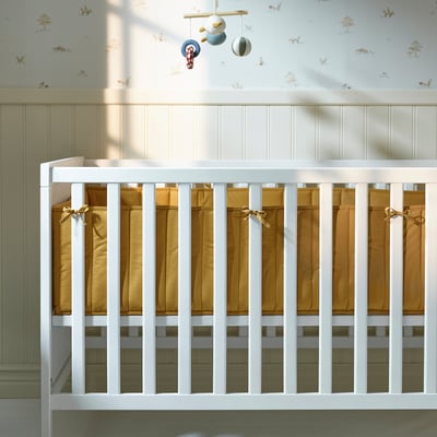 White wooden crib with tan padded sides, decorative ribbons and hanging mobile.