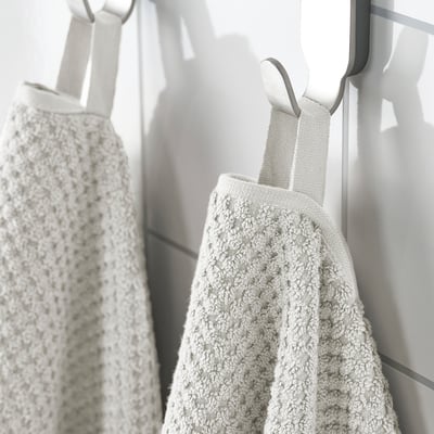 Two plush, beige cotton towels hang on hooks, one in focus, both featuring textured weave, demonstrating softness and absorbency.