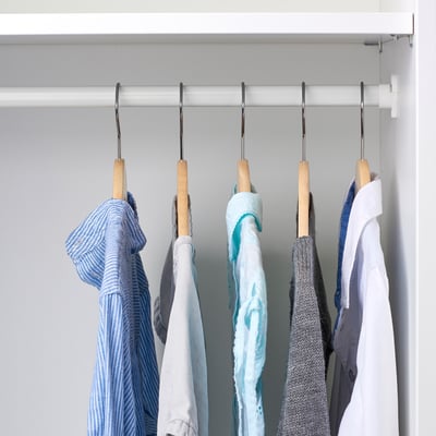 Closet with wooden hangers holding childrens clothes, organised neatly on a bar.