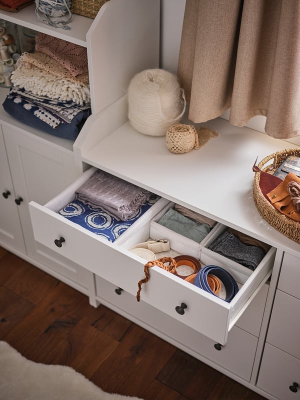 A white HAUGA storage unit with open drawers and various textiles on top.