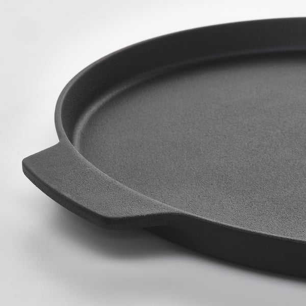 Black cast iron pizza pan with two handles, sitting on a white surface.
