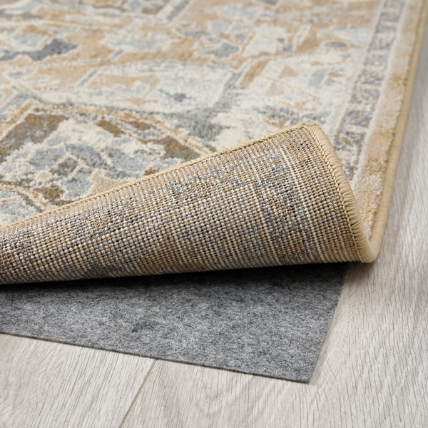 Rolling beige area rug, showing durable plush texture and non-slip rubber backing.