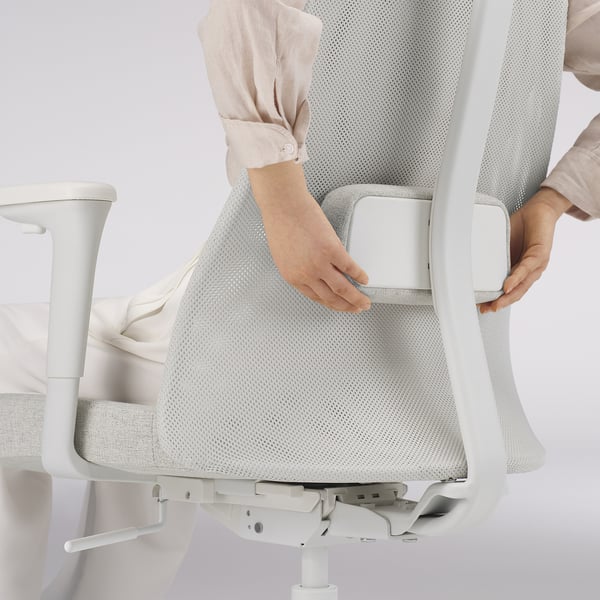 Adjusting lumbar support on ergonomic office chair. Person securing lumbar support under mesh back.