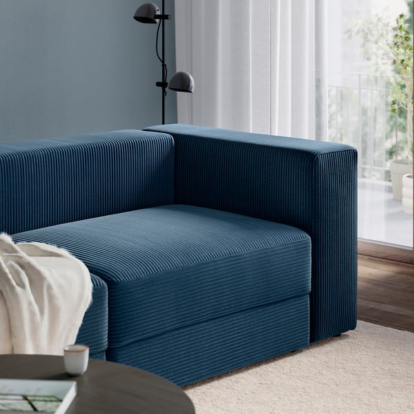 Modern blue corduroy sofa with smooth edges, next to a lamp, offering comfort and style.