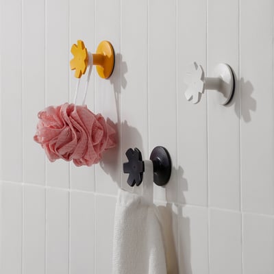 Three colourful snowflake hooks hang items in a bathroom. One holds a pink loofah, another a white towel. Easy-to-attach, practical storage.