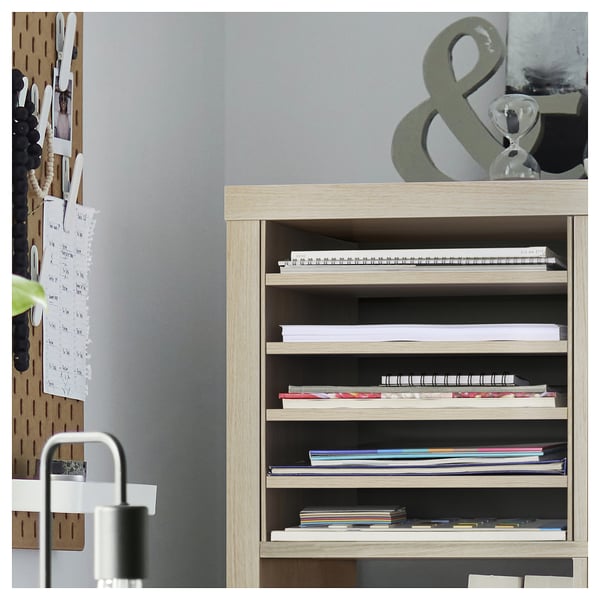KALLAX bookshelf with books & papers, grey wall, pegboard with notes.