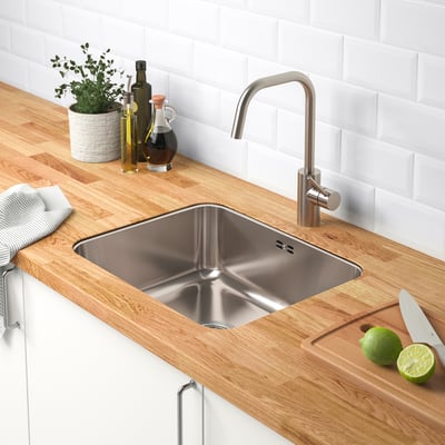 Modern kitchen sink area with stainless steel sink, wooden countertop, silver tap, limes, knife, and bottles.
