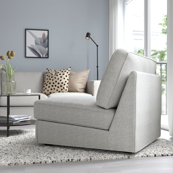 Modern living room: grey sofa bed with pillows sits near window; floor lamp, side table, vase with flowers.