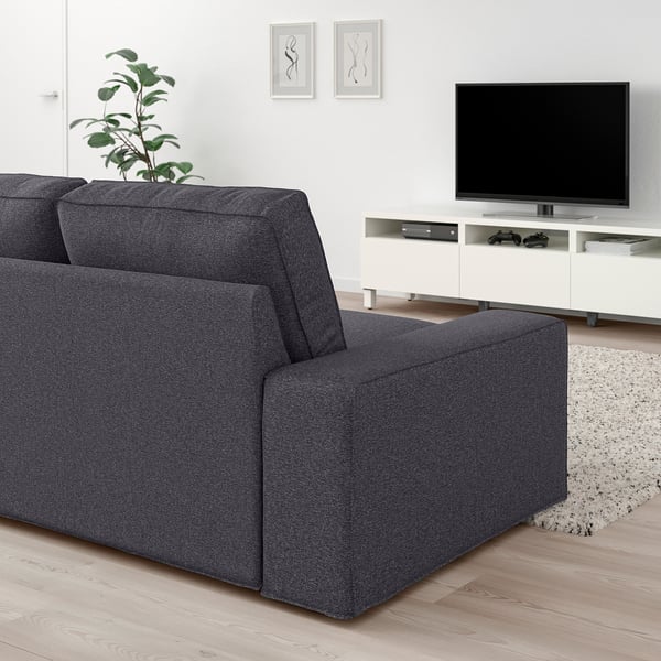 Modern living room with large grey KIVIK sofa, white tv stand, and flat screen tv. Sofas size dominates space with minimalist decor.