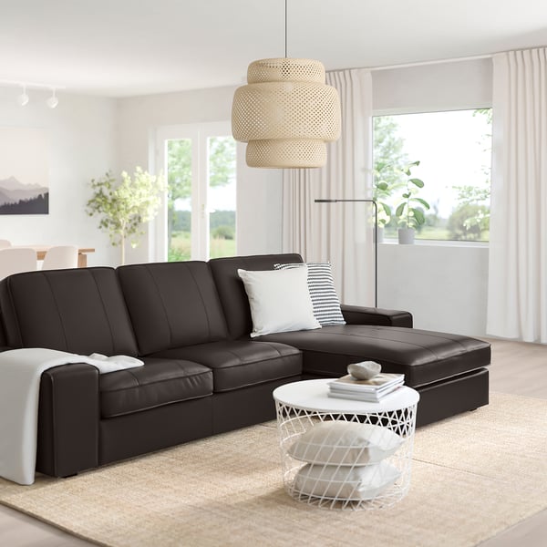 Modern living room with large black KIVIK sofa, white coffee table, hanging lamp, and large window with curtains.
