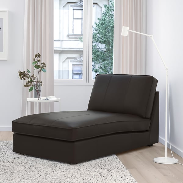 Modern living room with black KIVIK chaise longue, floor lamp, and side table. Large window with soft curtains behind.