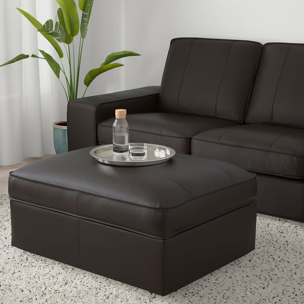 Modern living room with KIVIK black leather sofa and ottoman; ottoman has a tray with a bottle and glass, plant nearby.