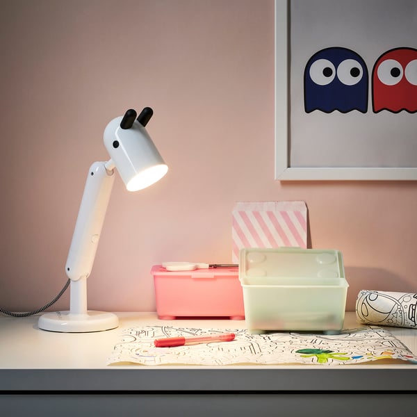 KRUX lamp, white, adjustable. Small, rounded body, flexible arm. On a desk with crafts.