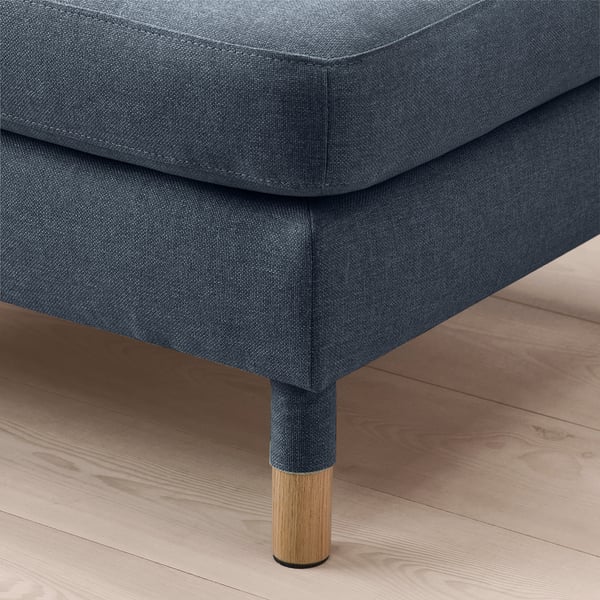 Modern grey fabric footstool with wooden legs on wooden floor.
