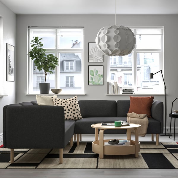 Modern living room with LILLEHEM sofa, rug, coffee table, plant, pendant light, city view.