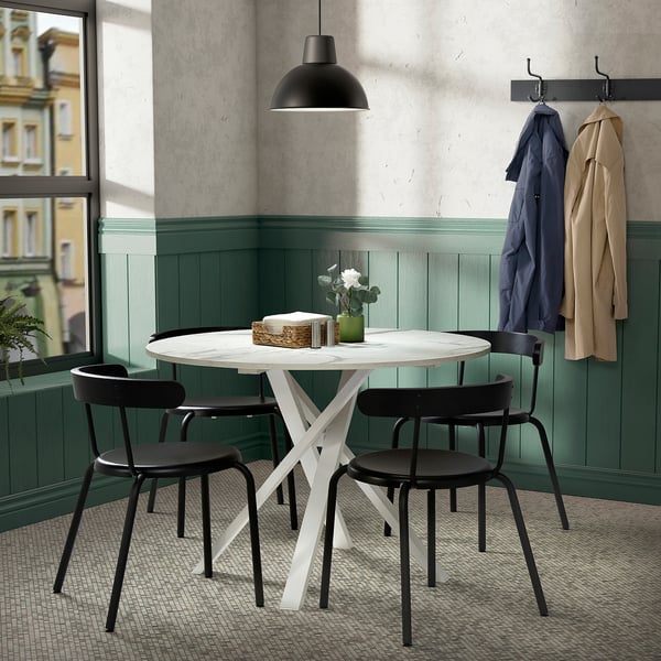 Cosy room with mariam table & black chairs near window. Two coats hang, light fixture adds modern touch.